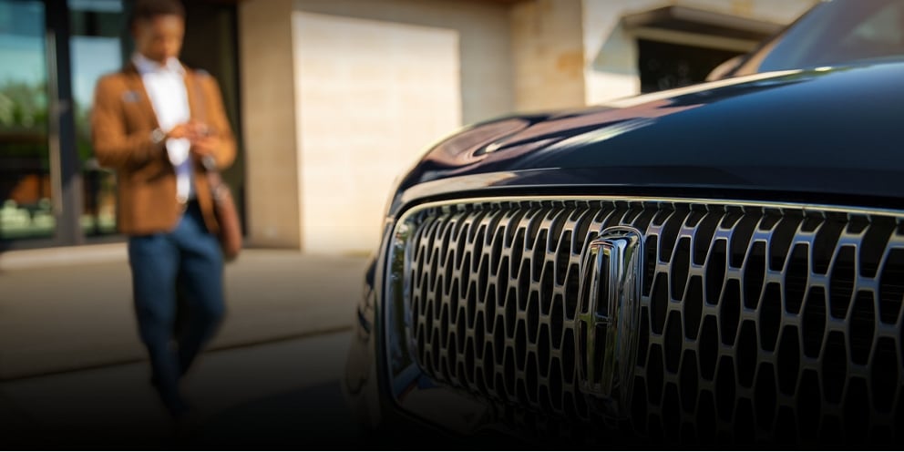 A person approaches a Lincoln vehicle while using a smartphone