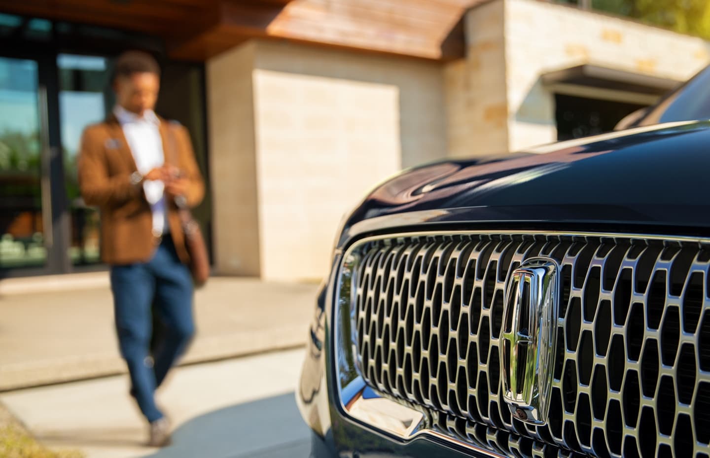 A person approaches a Lincoln vehicle while using a smartphone