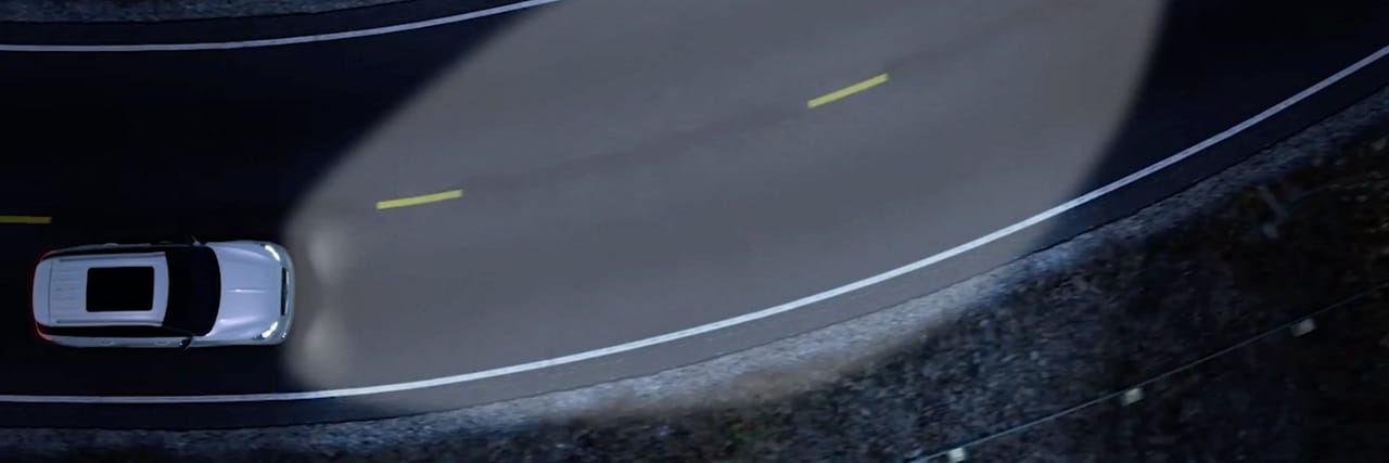 a Lincoln vehicle driving along a curve with headlights at night is shown here