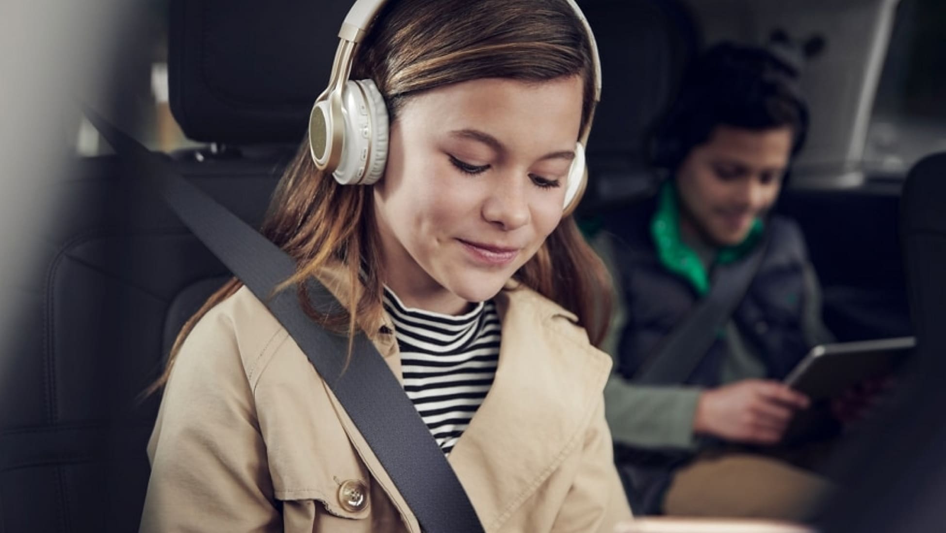Two children are wearing headphones and looking at mobile devices as passengers in a Lincoln SUV.