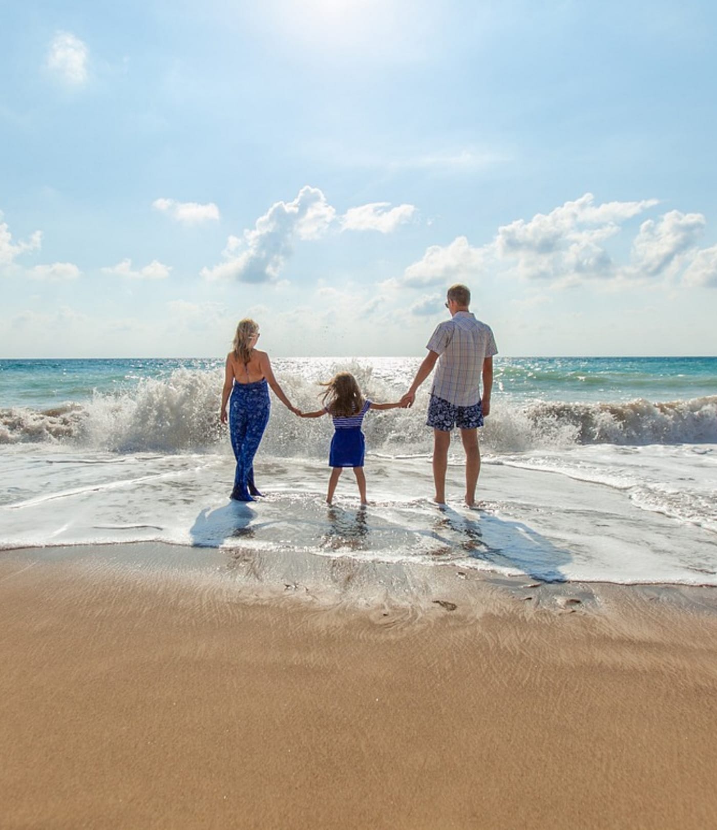 A family standing in the sand on the beach facing the water.
