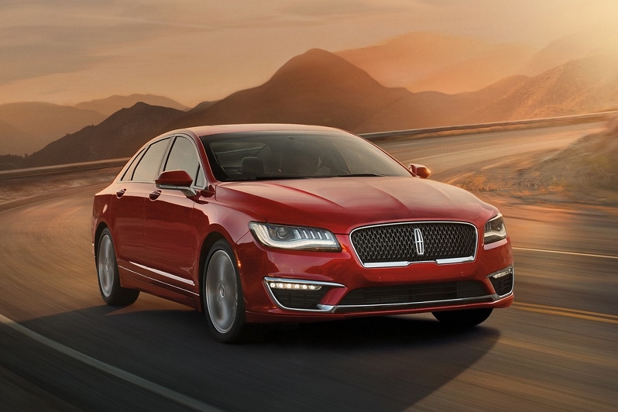 Un Lincoln MKZ andando por un camino de montaña con curvas en el brillo naranja de la luz del amanecer