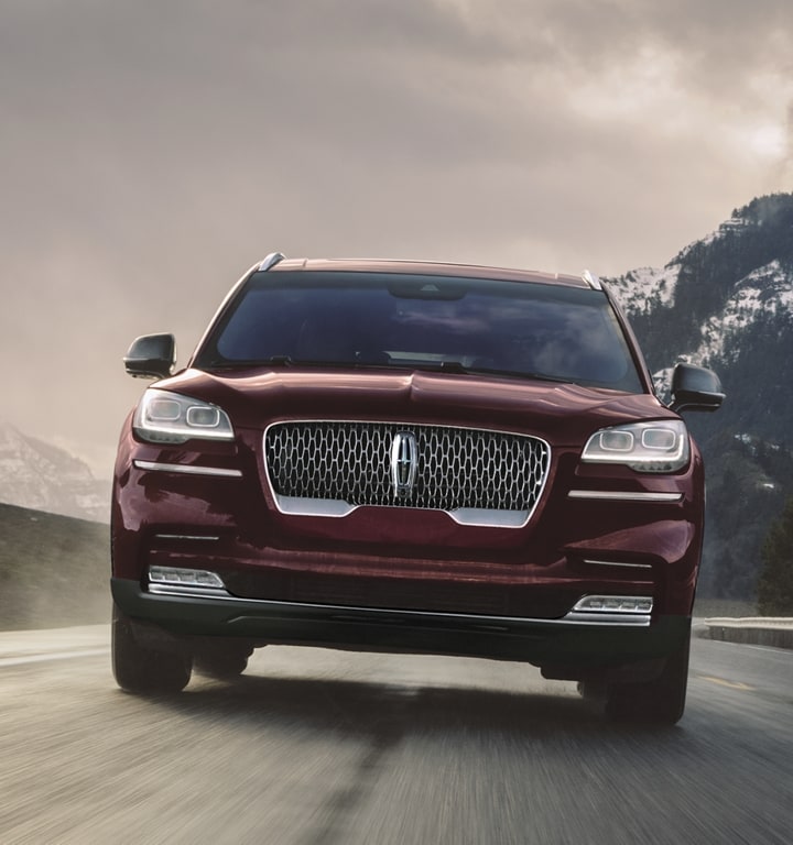 Se muestra una vista frontal directa de una Aviator Grand Touring andando por una carretera con cielo tenue y montañas oscuras de fondo
