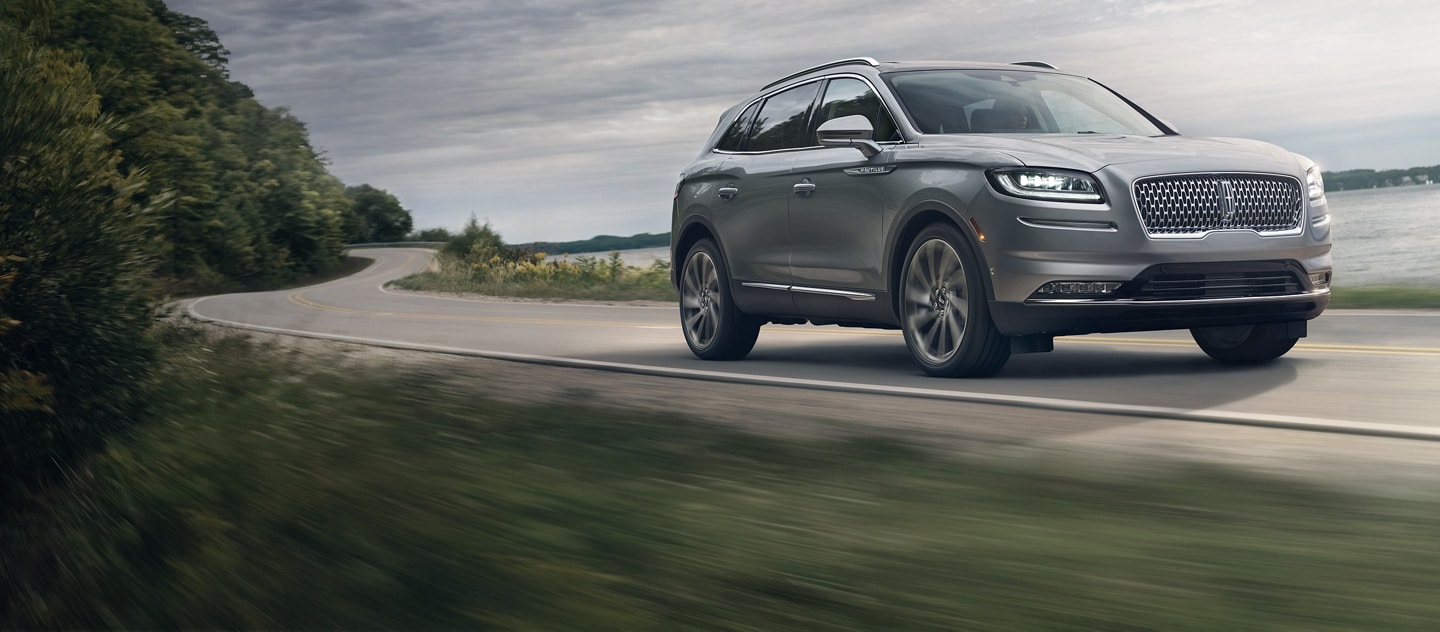A 2021 Lincoln Nautilus is shown being driven on a lakeshore roadway