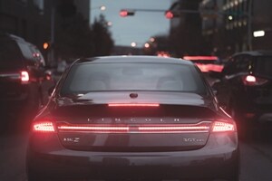 A Lincoln M K Z is stopped at a light in heavy traffic as the red brake lights and traffic light illuminate brightly in the night