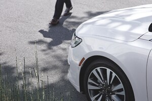 A man is walking in front of a white Lincoln vehicle that is stopped to allow him to cross