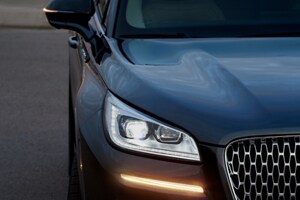 The front end of a Lincoln vehicle shows illuminated headlights and a turn signal that shines bright in the night