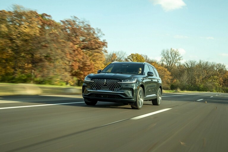 A 2026 Lincoln Aviator® SUV is shown driving on a tree-lined road