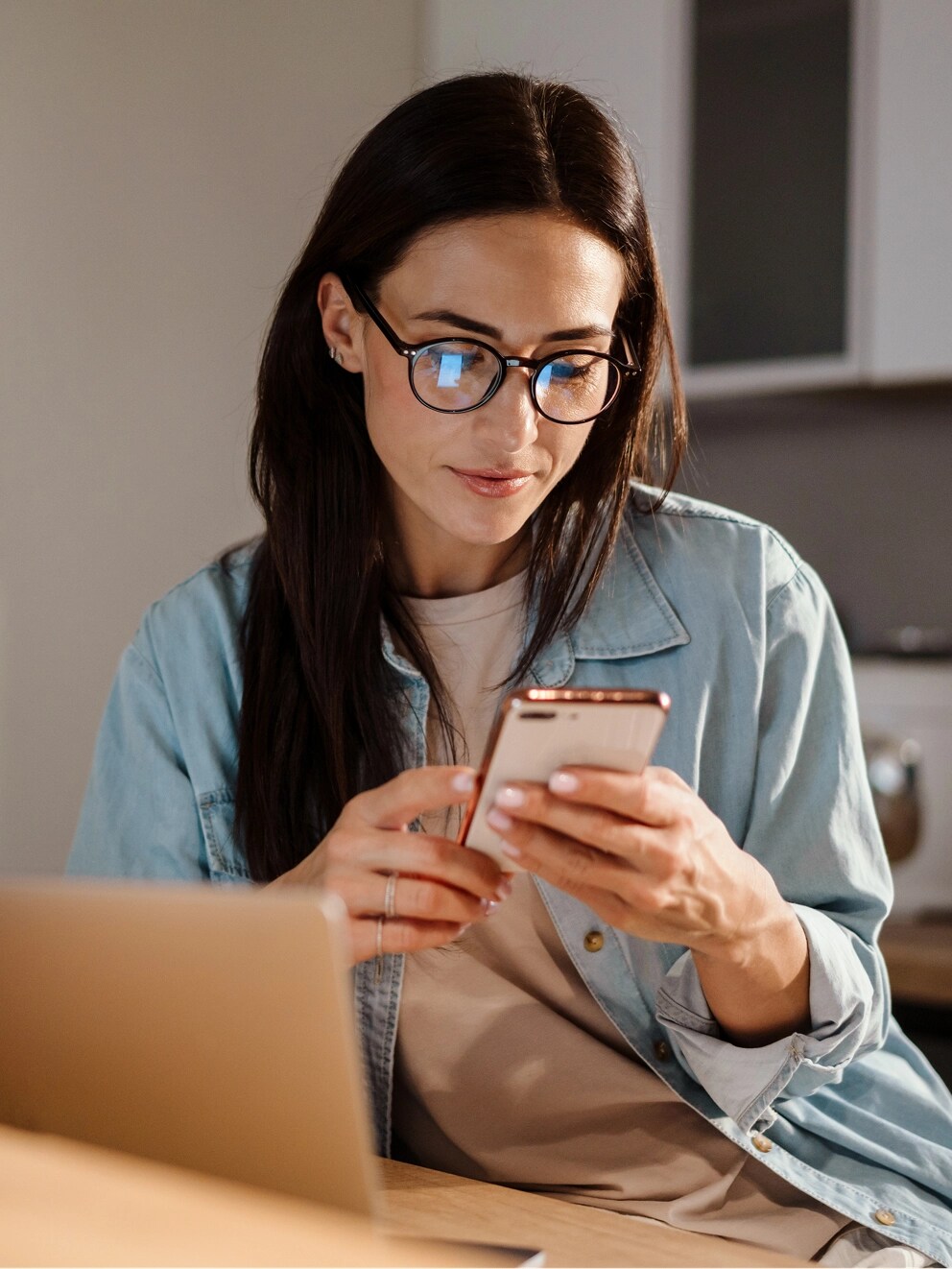 A woman sitting at a desk and looking at a cell phone.