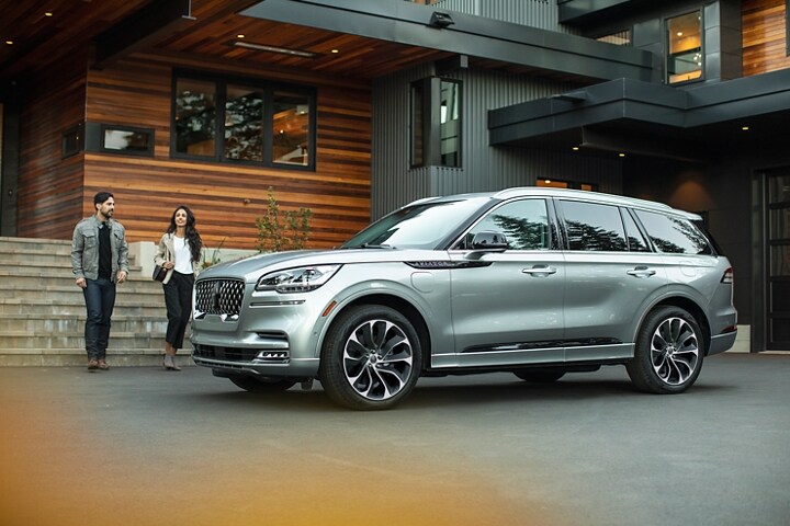 Una pareja se acerca a una Lincoln Aviator® Grand Touring 2023 estacionada en la entrada de una casa moderna