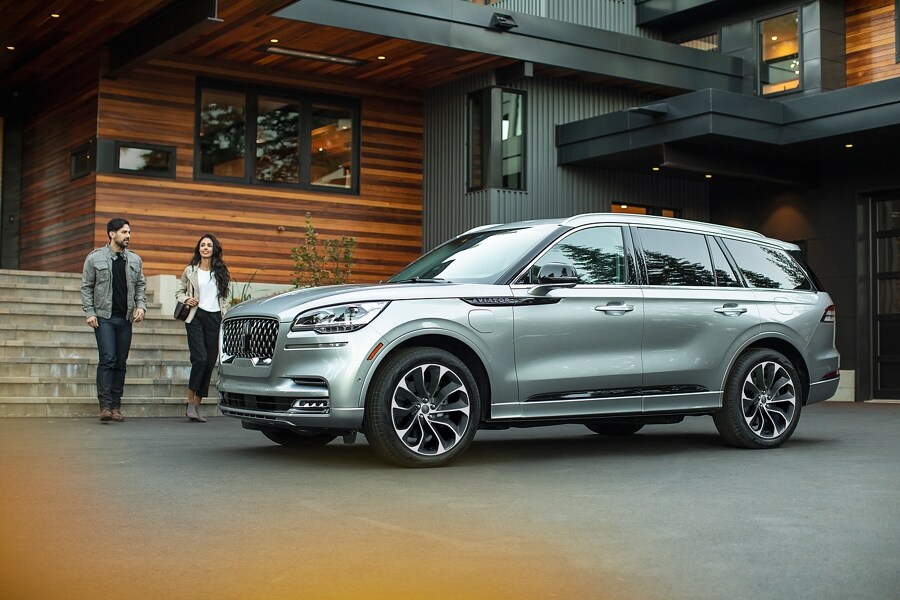 Two people are shown approaching a 2023 Lincoln Aviator® Grand Touring model that is parked in the driveway of a modern home