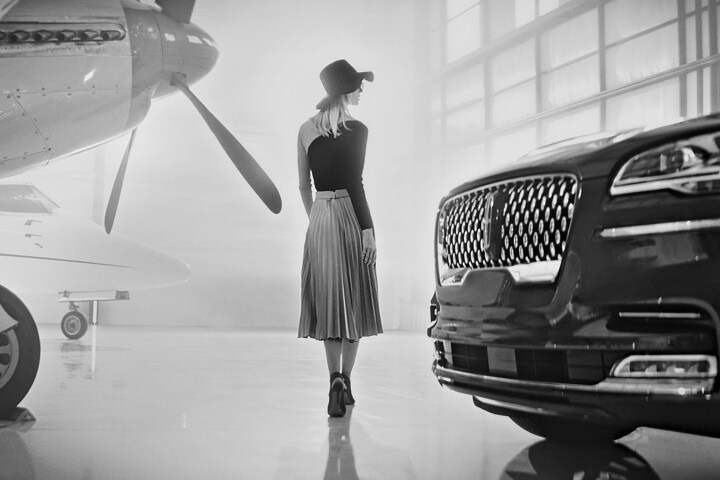 Una imagen en blanco y negro muestra a una mujer caminando por un hangar para aviones al lado de un modelo Lincoln Aviator® Black Label 2023