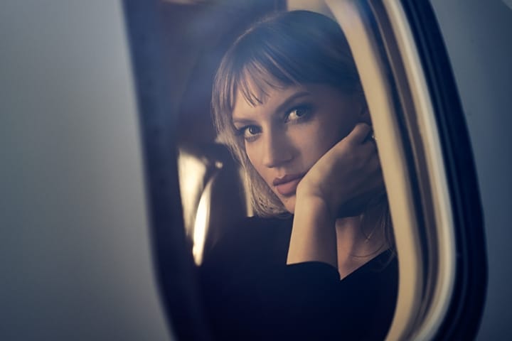 A woman is shown gazing through the window of a private jet