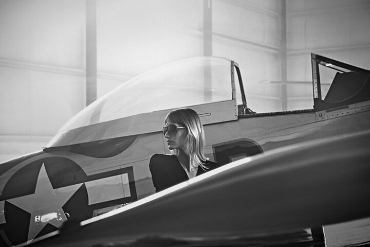 Imagen de una mujer de pie junto a un avión de combate antiguo en un hangar privado