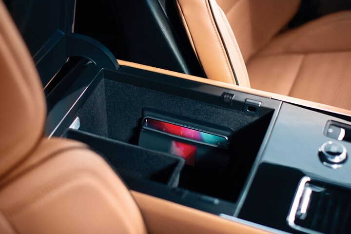 Se muestra el compartimento de almacenamiento de una SUV Lincoln Aviator® 2023 abierto con un teléfono conectado en el cargador inalámbrico disponible