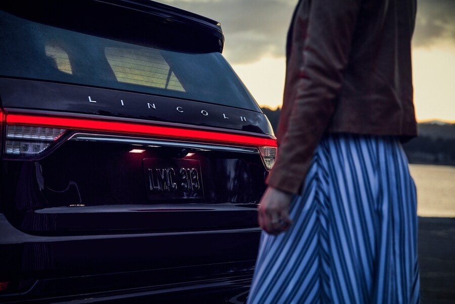A person is shown approaching the rear of a 2023 Lincoln Aviator® which has the taillamps illuminated