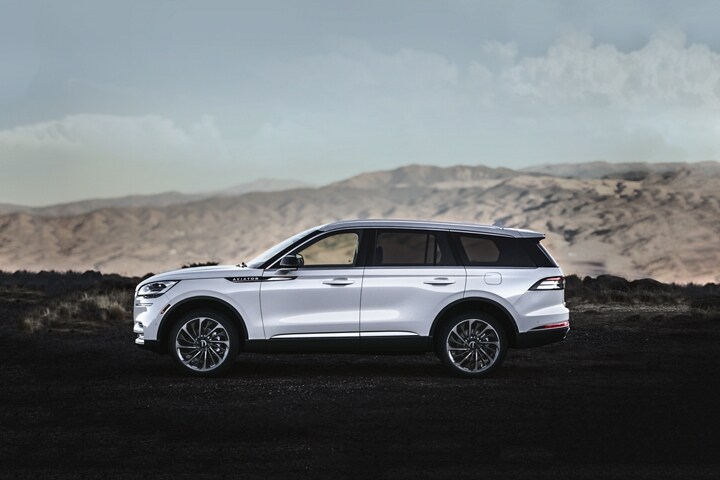 Imagen de una Lincoln Aviator® 2023 de color exterior blanco inmaculado estacionada sobre un bello paisaje montañoso