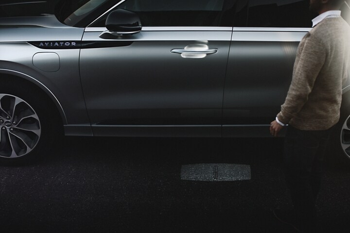 Una persona se acerca a una Lincoln Aviator® Grand Touring 2023 mientras se ilumina la secuencia de luces de Lincoln Embrace.