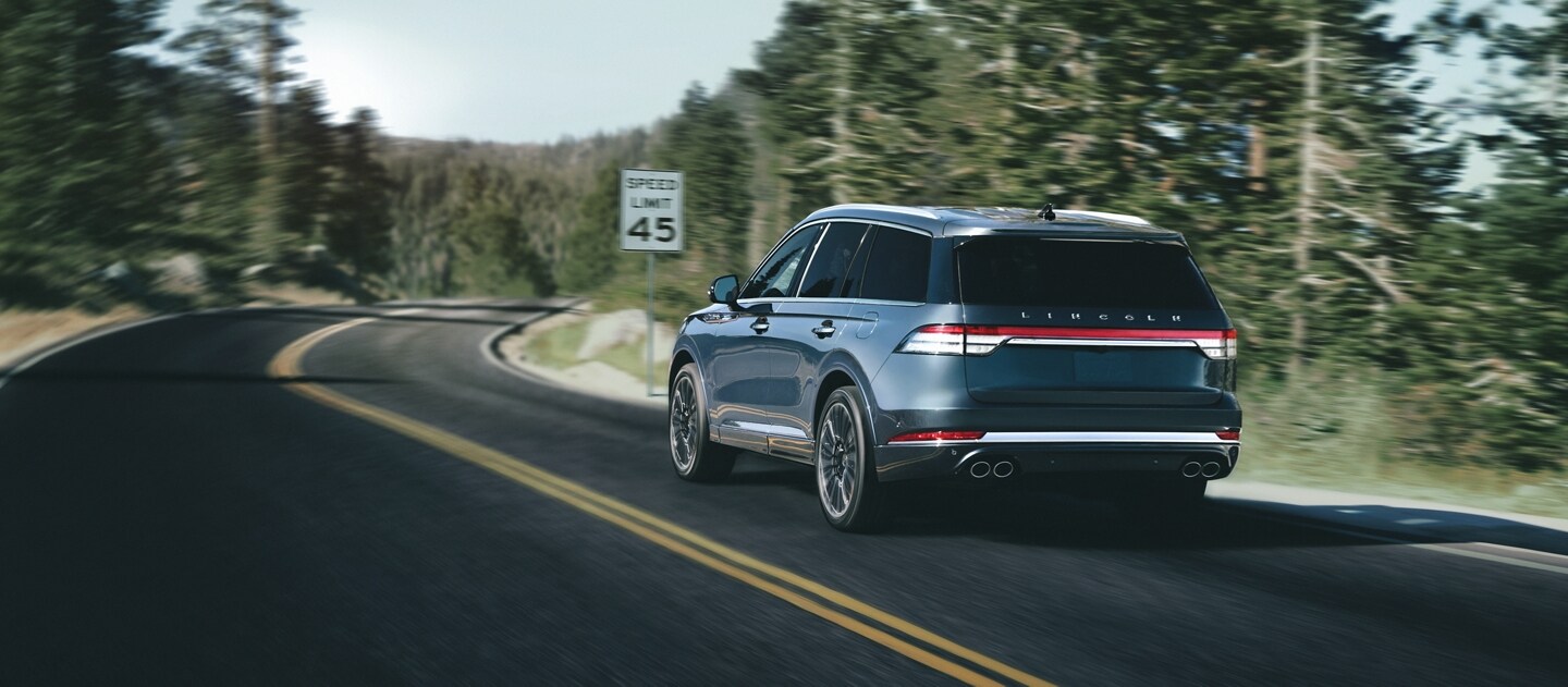 A 2023 Lincoln Aviator® is shown being driven on a winding road as it approaches a speed limit sign