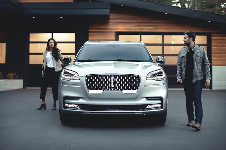 A couple is shown leaving a 2023 Lincoln Aviator® Grand Touring model in the driveway of a modern home