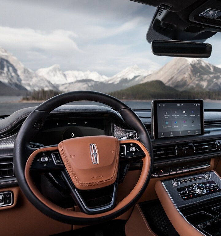 The steering wheel of a 2023 Lincoln Aviator® is featured with snow-capped mountains shown through the windshield