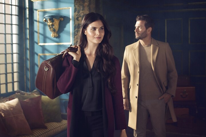 Se muestra una pareja que lleva equipaje hacia el vestíbulo de un hotel lujoso para representar la inspiración del tema Destination