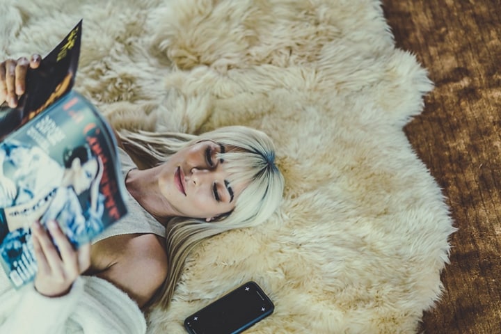 Se muestra una mujer descansando con una revista sobre un tapete cómodo y cálido