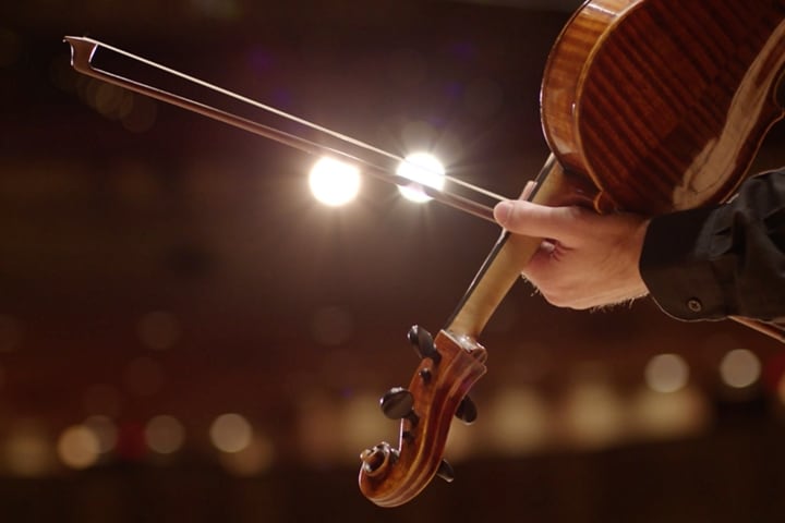 A bow is shown sliding across the strings of a violin