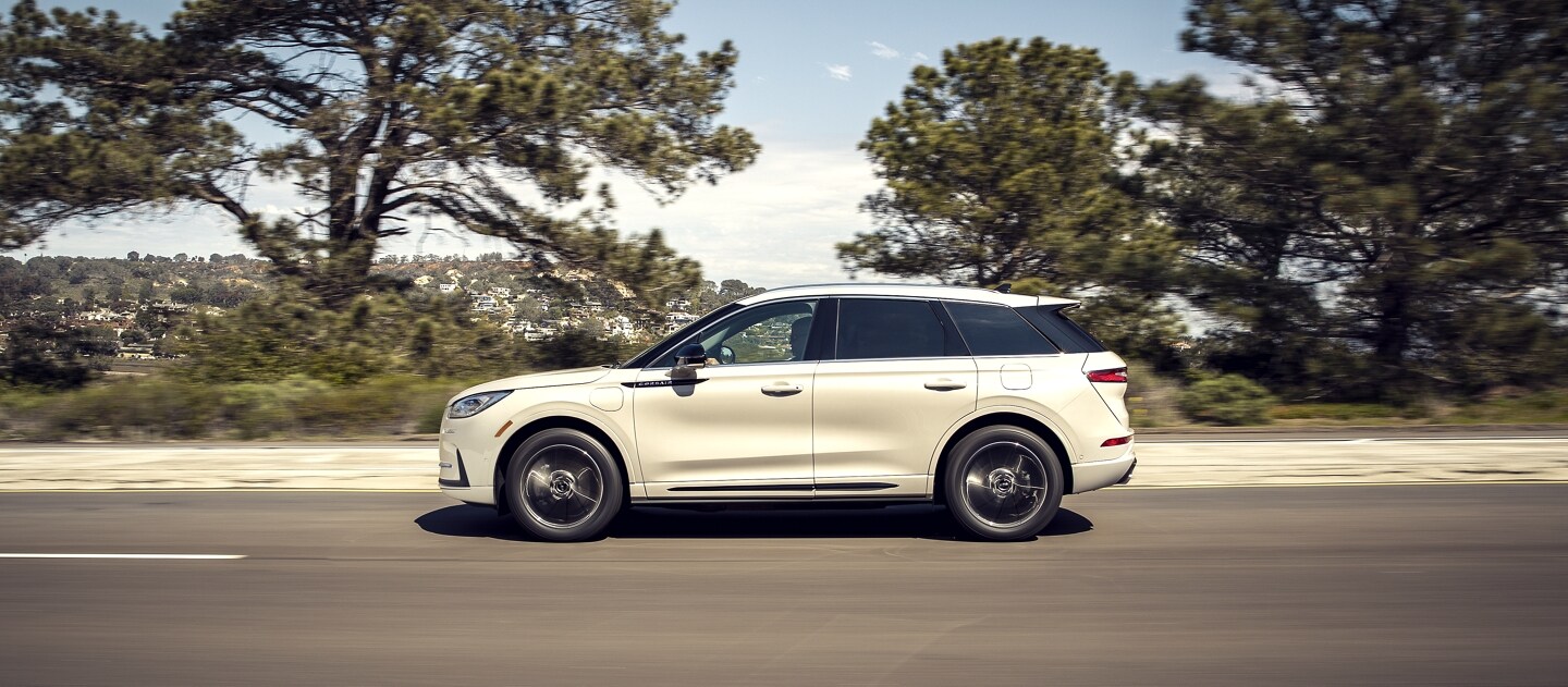 Un modelo Lincoln Corsair® Grand Touring 2023 andando por una costa con vegetación