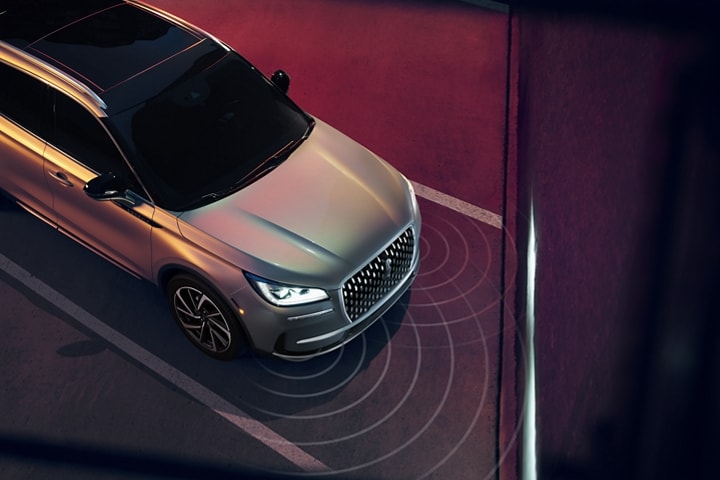 A 2023 Lincoln Corsair® SUV is being guided into a diagonal parking space as the headlamps illuminate the wall ahead
