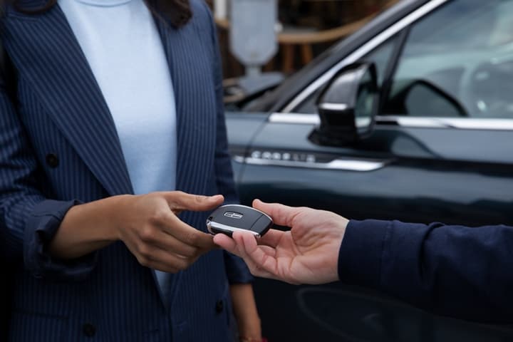 A Lincoln service representative hands a woman a key during pick up and delivery service