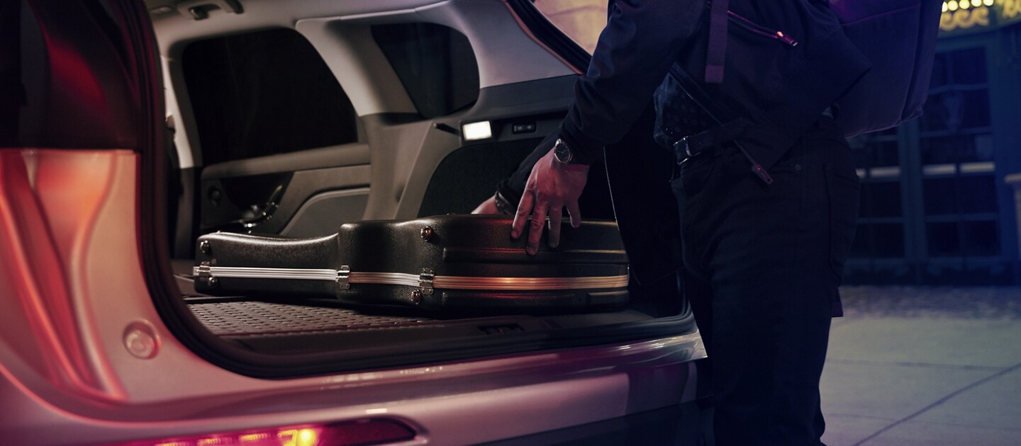 Un músico guarda el estuche de su guitarra en la zona de carga de una SUV Lincoln Corsair® 2024 con los asientos traseros plegados