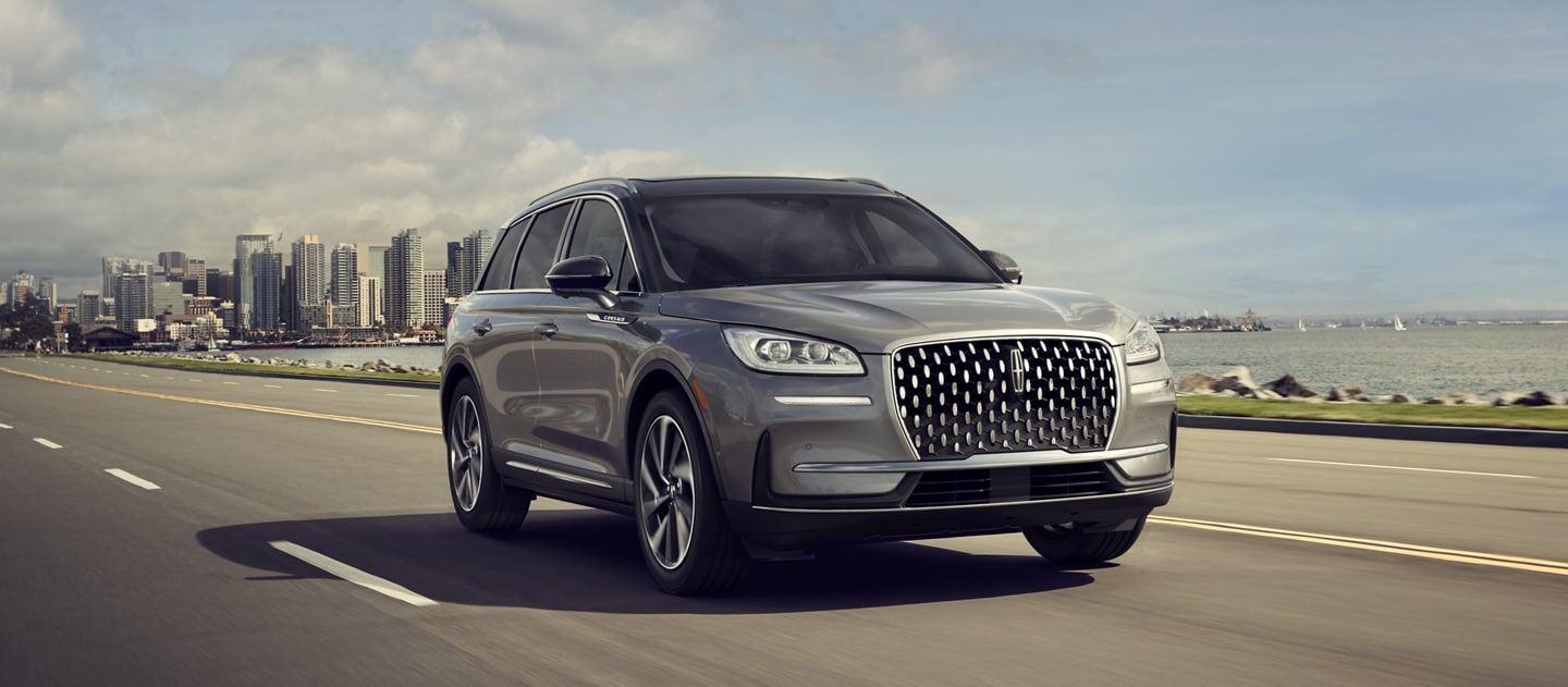 A 2024 Lincoln Corsair® SUV is being driven along a waterfront road with a city skyline in the background