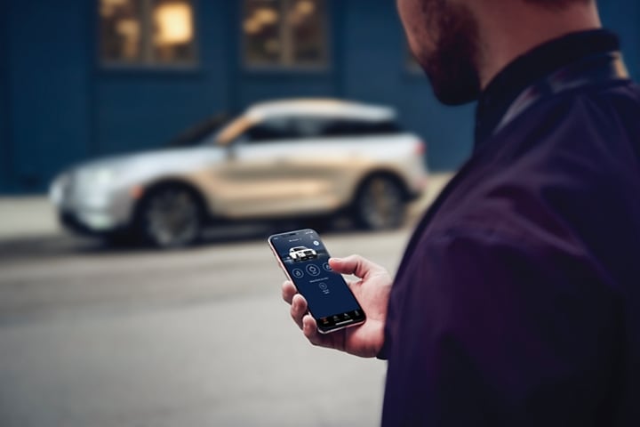 Un hombre parado en la calle de enfrente de su vehículo Lincoln interactuando con la aplicación Lincoln Way® en su smartphone