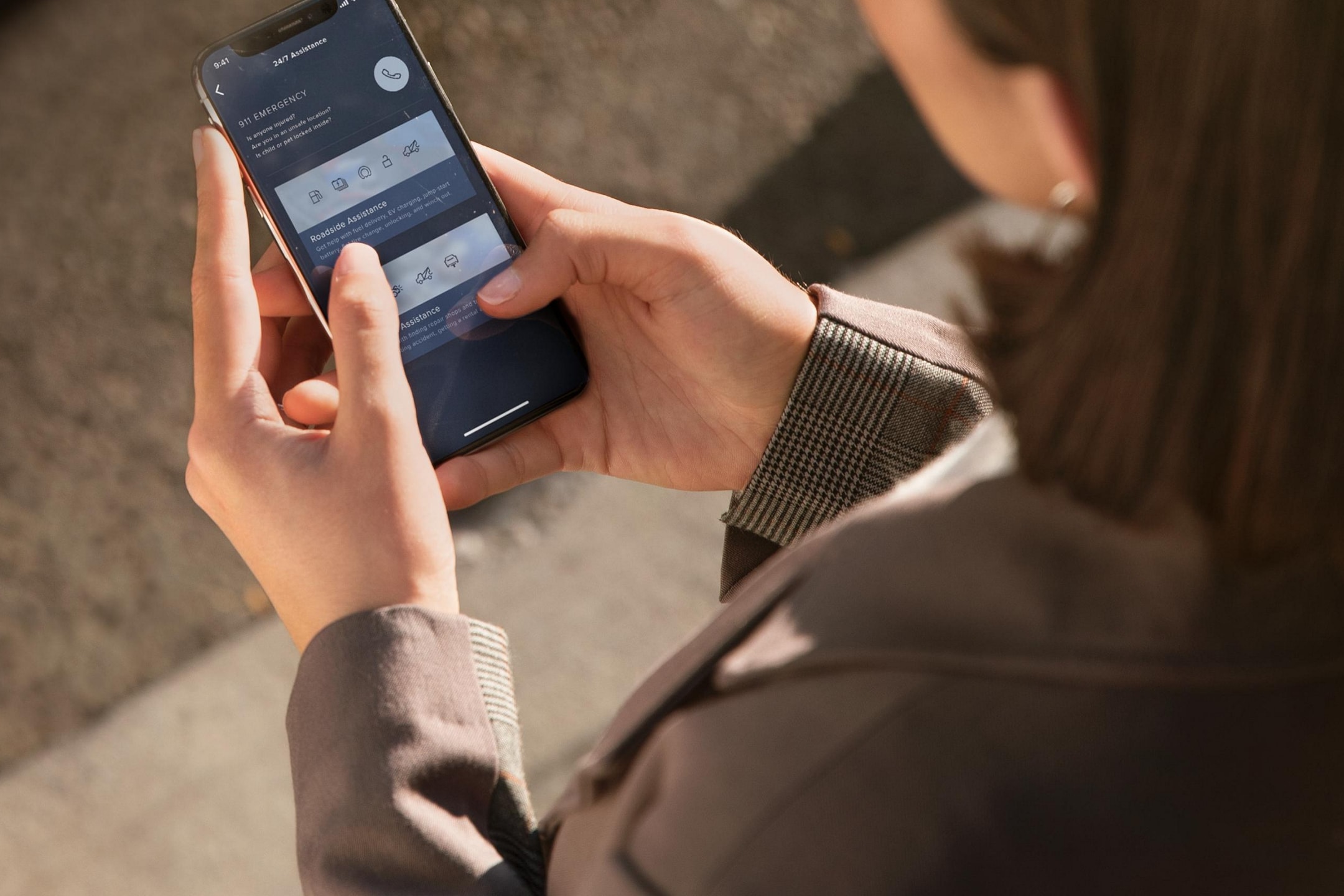 A woman is standing across from her Lincoln vehicle interacting with the Lincoln Way® App on her smartphone device