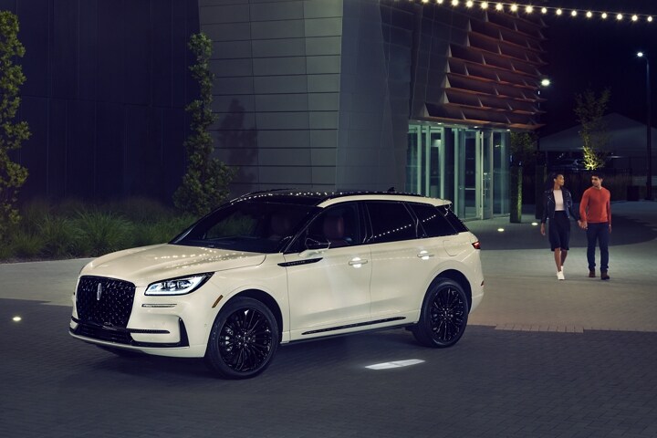 Una pareja acercándose a una SUV Lincoln Corsair® 2024 en una noche, recibida por el suave brillo suave de Lincoln Embrace