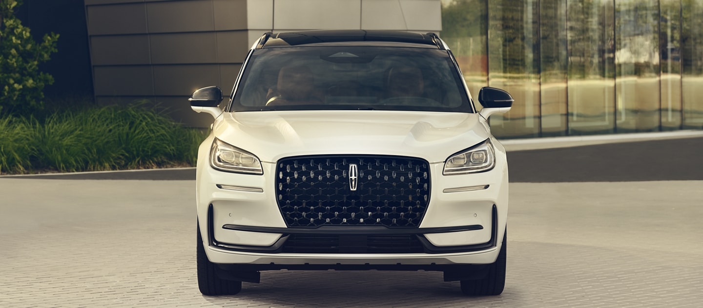 La parrilla de una Lincoln Corsair® 2024 con el paquete de apariencia Jet disponible que está estacionada frente a un edificio moderno