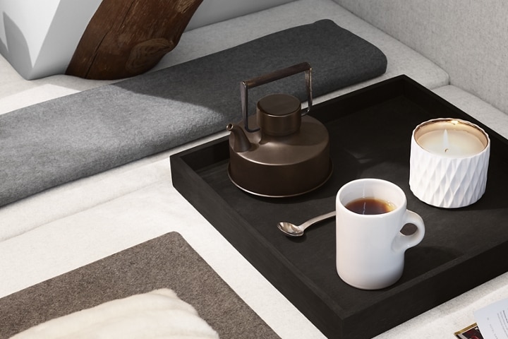 Se muestra una tetera, una taza de té y una vela encendida sobre una bandeja de té para reflejar la naturaleza calma del tema Chalet