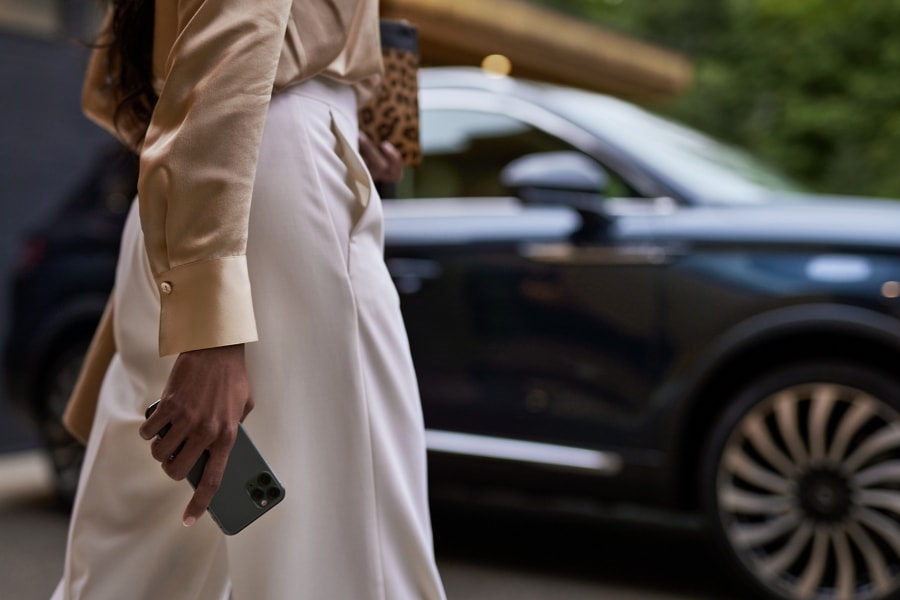 Una mujer sostiene un smartphone en la mano mientras camina hacia una SUV Lincoln Black Label Nautilus® 2023