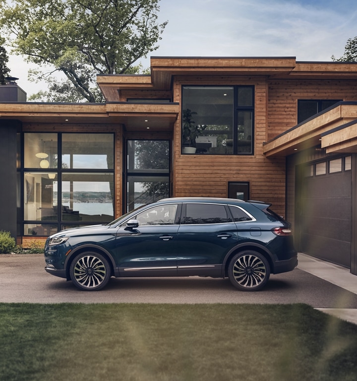Un modelo Lincoln Nautilus® Black Label 2023 en azul flight estacionada afuera de una casa moderna junto a un lago