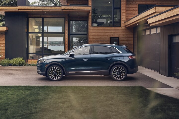 Una SUV Lincoln Black Label Nautilus® 2023 estacionada afuera de una casa moderna junto a un lago
