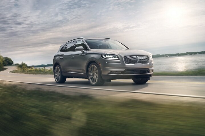 Una SUV Lincoln Nautilus® 2023 en plateado radiante circulando por un camino junto a un lago