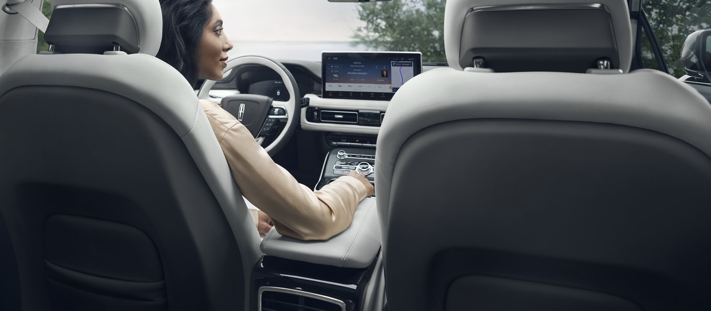 A woman is sitting in the driver’s seat of a 2023 Lincoln Nautilus® SUV parked overlooking a lake