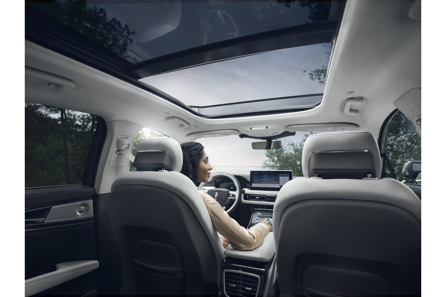Una mujer está sentada en el asiento del conductor de una SUV Lincoln Black Label Nautilus® 2023 estacionada mirando un lago