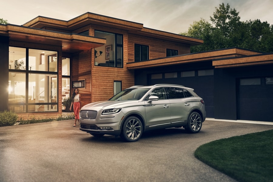 A person approaches a 2023 Lincoln Nautilus® SUV in Silver Radiance parked outside a mid-century modern home