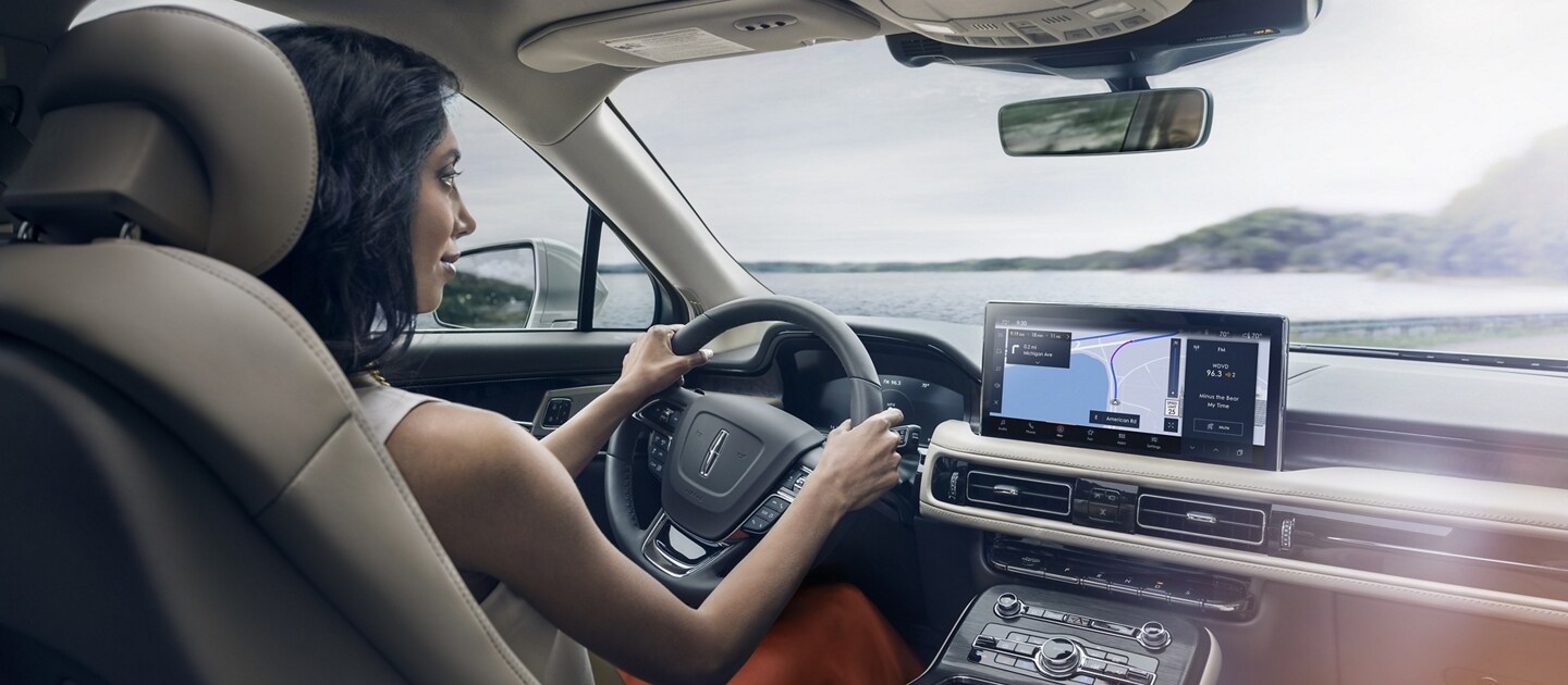 Una mujer conduce una SUV Lincoln Nautilus® 2023 mientras la aplicación de navegación en la pantalla táctil central guía su curso