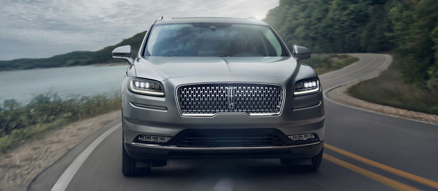 La parte delantera de la SUV Lincoln Nautilus® 2023 se muestra andando en una curva en una carretera junto al lago