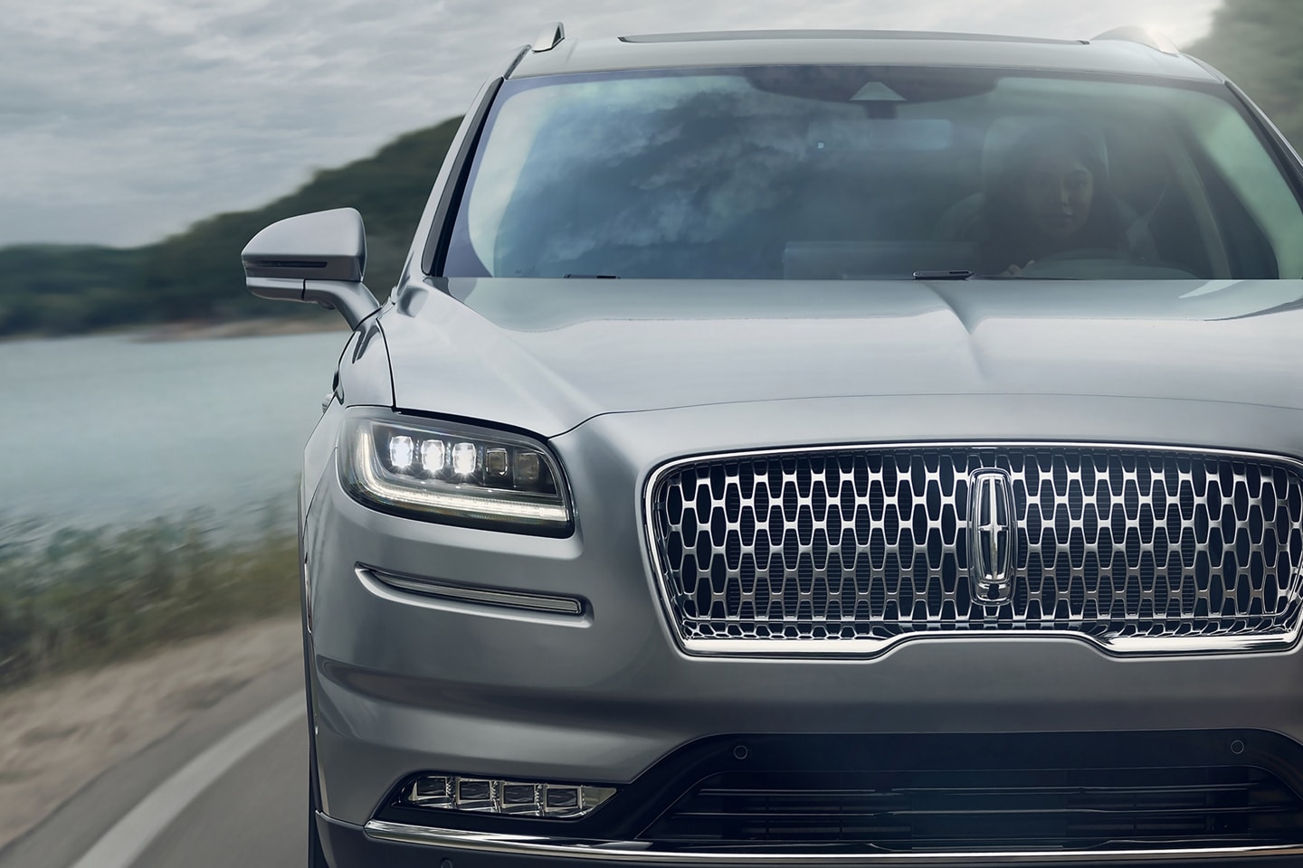     The front end of the 2023 Lincoln Nautilus® SUV is being driven around a curve in a lake side road