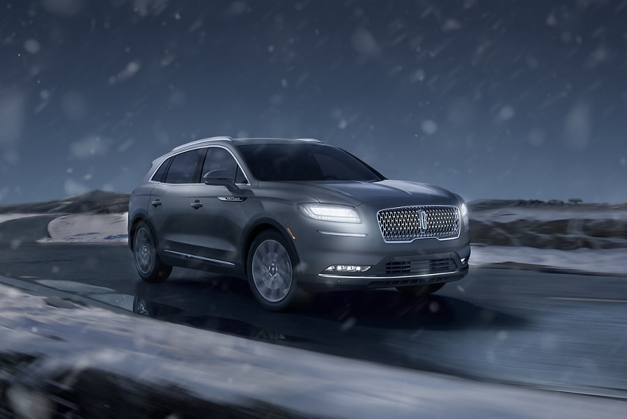 Imagen de nieve que cae en el haz de luz de los faros delanteros de una SUV Lincoln Nautilu​​​​​​​s® 2023 mientras pasa por una carretera nevada