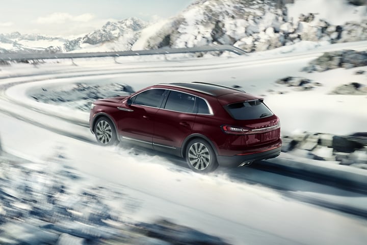 A 2023 Lincoln Nautilus® SUV is shown being driven on a snow covered road with a sharp turn ahead
